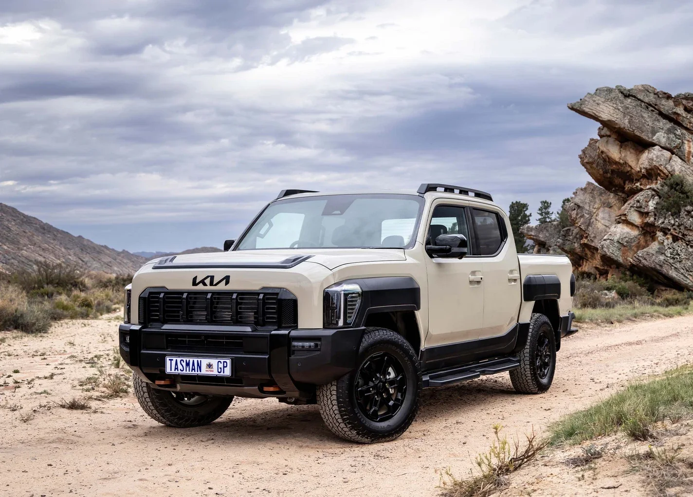 Sand-coloured Kia Tasman bakkie on a gravel track among rocks